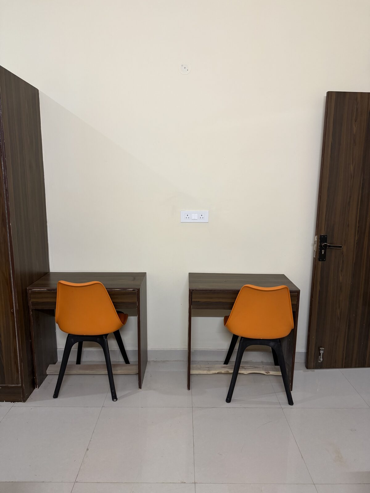 Hostel room study corner with two wooden desks and orange chairs